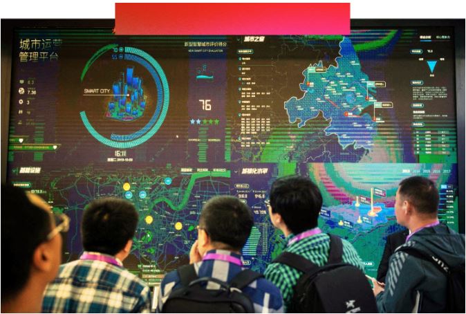 بازدیدکنندگان در نمایشگاه بین‌المللی امنیت و امنیت عمومی چین در سال 2018، به یک برنامه نرم‌افزار امنیتی هوش مصنوعی روی صفحه‌ای پر از نمودارها و گرافیک‌هایی با متن به حروف چینی نگاه می‌کنند.